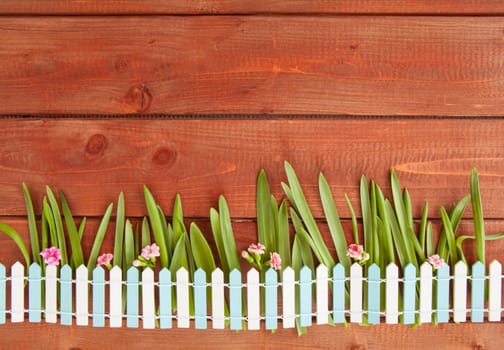 Kleienr garden fence with grass and flowers on a rustic wooden background