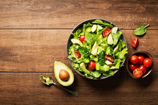 Green salad with avocado and fresh vegetables on wooden background.