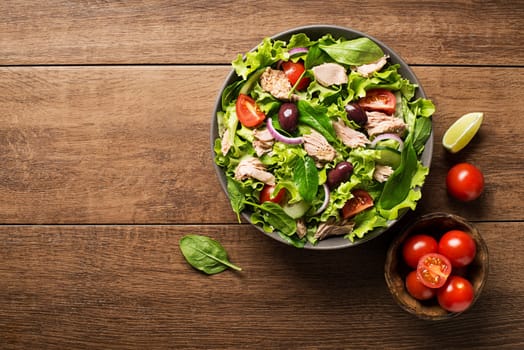 Tuna salad with lettuce, tomatoes and olives on wooden table