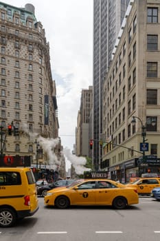 New York, NY, USA - June 06, 2015:Steam coming out of Greeley Square and the intersection West 32 in Manhattan in the spring. Traffic of cars and crowds of people.