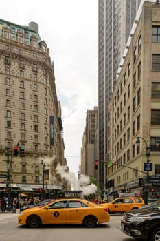 New York, NY, USA - June 06, 2015:Steam coming out of Greeley Square and the intersection West 32 in Manhattan in the spring. Traffic of cars and crowds of people.