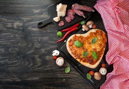 Heart-shaped pizza Margherita with fresh ingredients on a rustic wooden background