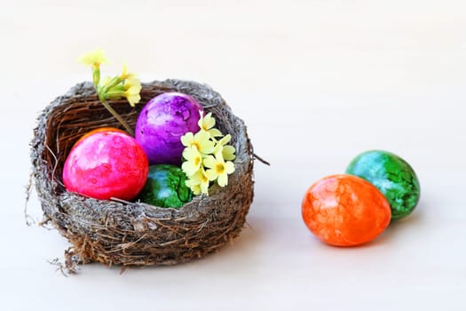 An Easter nest with colorful Easter eggs on a light wooden background