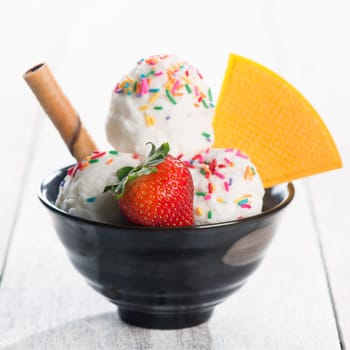 Vanilla ice cream in bowl with waffle on white rustic wooden background.