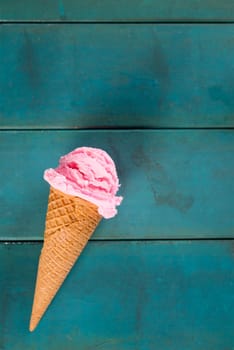 Top view strawberry ice cream waffle cone on blue wooden background, close up.