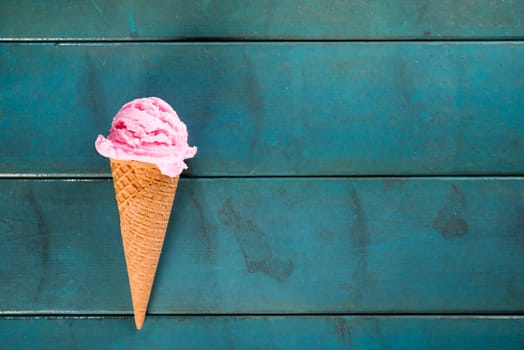 Top view strawberry ice cream waffle cone on blue wooden background, copy space on side.