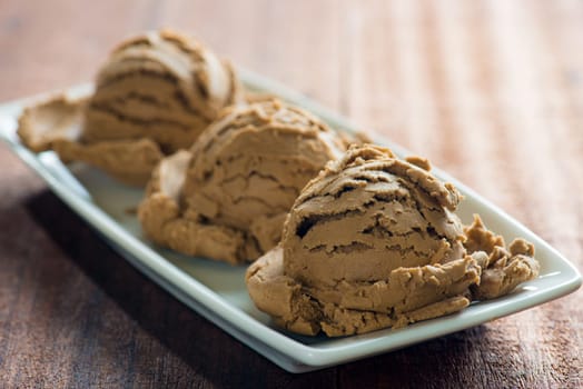 Brown ice cream in plate on dark wood background.