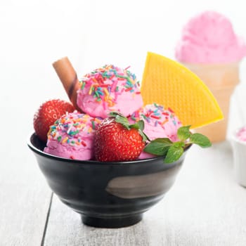 Pink ice cream in bowl with strawberry fruits and waffle on white rustic wooden background.