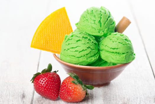 Scoop of matcha ice cream in bowl on wooden background.