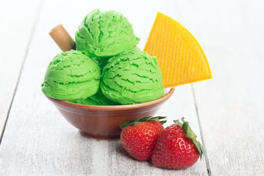 Scoop of honeydew ice cream in bowl on wooden background.