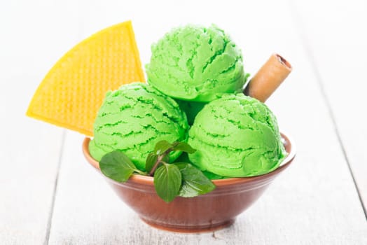Scoop of pistachio ice cream in bowl on wooden background.