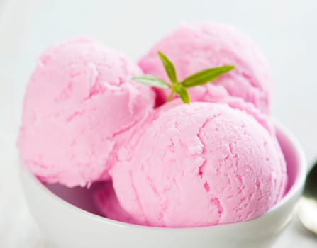 Pink berry ice cream in bowl on white wooden background.