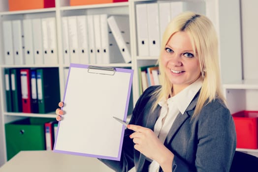 young blond business woman in the office pointing at clipboard