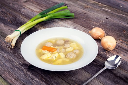 marrow balls soup in white plate with onion on wooden ground