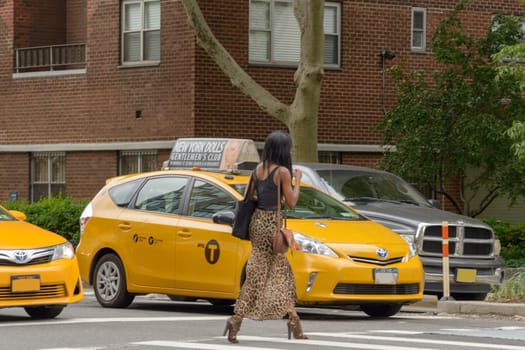 New York City, USA - June 08, 2017: New York yellow taxi cab stop at pedestrians traffic lights crossing the street in pedestrian crossing. American woman crosses the zebra crossing while the taxis are stationary.