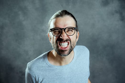 young man in front of gray background looking angry