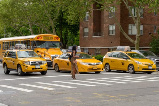 New York City, USA - June 08, 2017: New York yellow taxi cab stop at pedestrians traffic lights crossing the street in pedestrian crossing. American woman crosses the zebra crossing while the taxis are stationary.