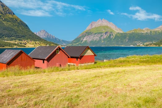 Beautiful landscape of Norway. Red barns, lake and meadows, mountains and cloudy sky in background. Travel in Scandinavia, Europe