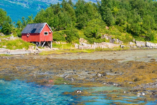 Beautiful landscape of Norway. Red barn, trees and water, mountains in background. Travel in Scandinavia, Europe.