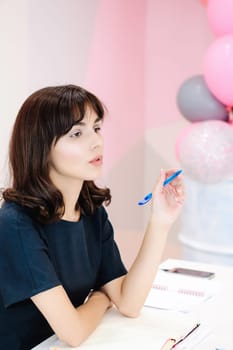 Portrait of a beautiful business woman making notes in a notebook. Holds a pen, sitting in the workplace in a pink office