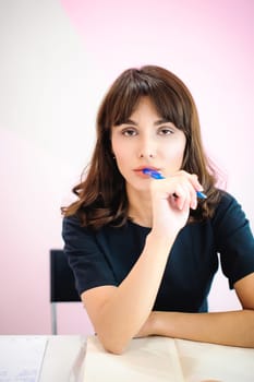 Portrait of a beautiful business woman making notes in a notebook. Holds a pen, sitting in the workplace in a pink office