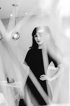 young woman in an elegant black dress with a phone in her hand, into a room with a pink interior and a fashionable lamp