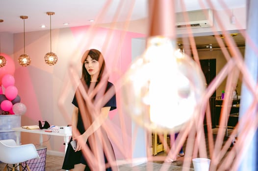 young woman in an elegant black dress with a phone in her hand, into a room with a pink interior and a fashionable lamp