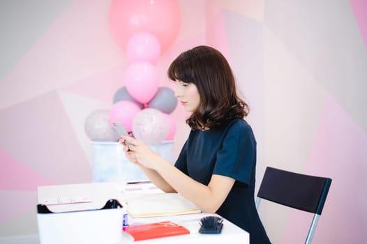 Portrait of a beautiful business woman making notes in a smartphone. Holding a cell phone while sitting in a workplace in a pink office