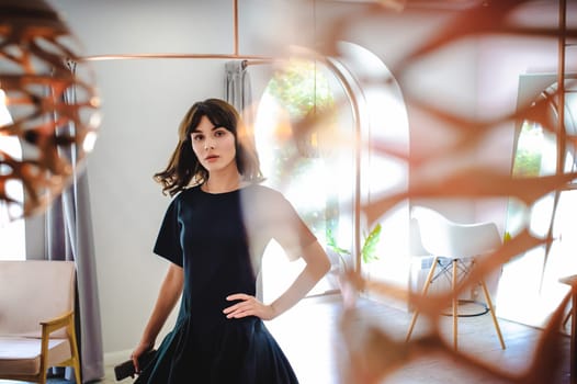 young woman in an elegant black dress with a phone in her hand, into a room with a pink interior and a fashionable lamp