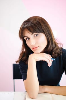 Portrait of a beautiful business woman making notes in a notebook. Holds a pen, sitting in the workplace in a pink office