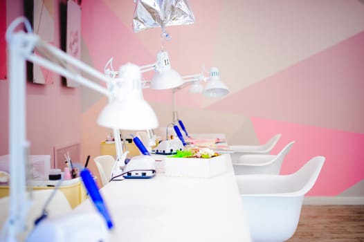 Workplace in a bright manicure salon. Working table of the master of nail service, chairs and lamps