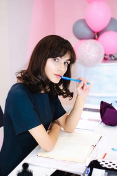 Portrait of a beautiful business woman making notes in a notebook. Holds a pen, sitting in the workplace in a pink office