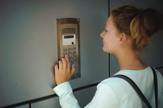 young blond teenager schoolgirl dials the code for a call over the intercom