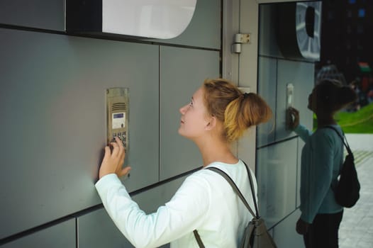 young blond teenager schoolgirl dials the code for a call over the intercom