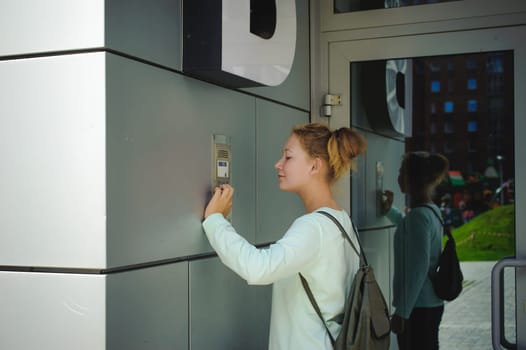 young blond teenager schoolgirl dials the code for a call over the intercom