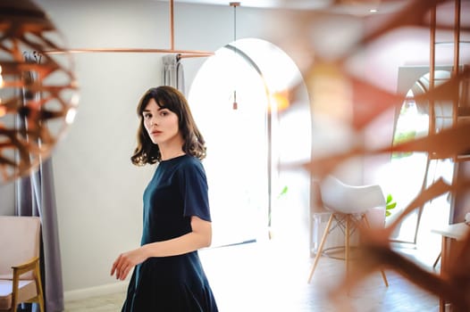 young woman in an elegant black dress with a phone in her hand, into a room with a pink interior and a fashionable lamp