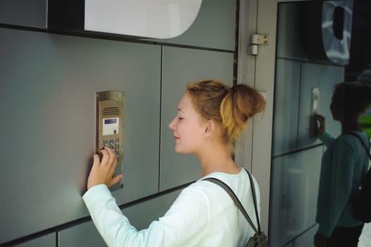 young blond teenager schoolgirl dials the code for a call over the intercom