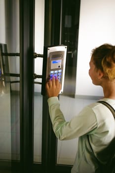 young blond teenager schoolgirl dials the code for a call over the intercom