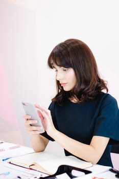 Portrait of a beautiful business woman making notes in a smartphone. Holding a cell phone while sitting in a workplace in a pink office