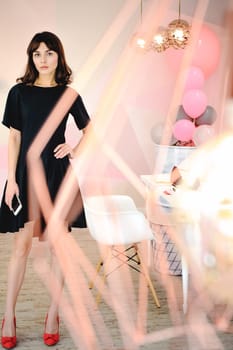 young woman in an elegant black dress with a phone in her hand, into a room with a pink interior and a fashionable lamp
