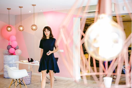 young woman in an elegant black dress with a phone in her hand, into a room with a pink interior and a fashionable lamp