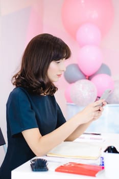Portrait of a beautiful business woman making notes in a smartphone. Holding a cell phone while sitting in a workplace in a pink office