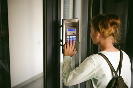 young blond teenager schoolgirl dials the code for a call over the intercom