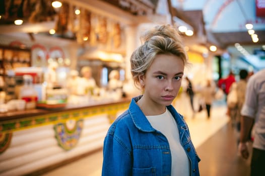 young beautiful woman in jeans clothes in business space of shopping center. portrait of a girl with freckles on her face, stylish girl standing near show-windows of fair in shopping center