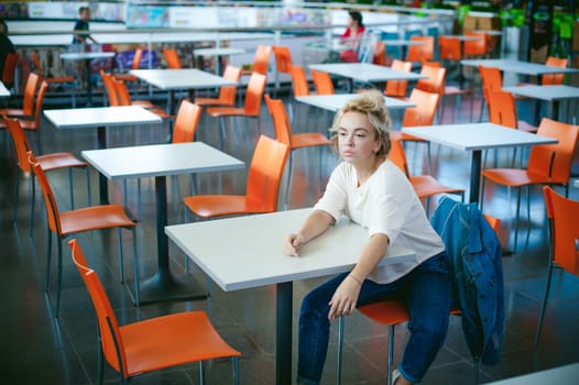 young beautiful woman in jeans clothes in business space of shopping center. portrait of a girl with freckles on her face, stylish girl in an empty cafe