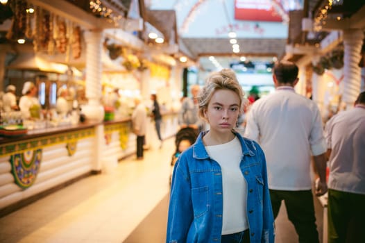 young beautiful woman in jeans clothes in business space of shopping center. portrait of a girl with freckles on her face, stylish girl standing near show-windows of fair in shopping center