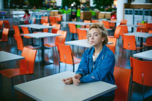 young beautiful woman in jeans clothes in business space of shopping center. portrait of a girl with freckles on her face, stylish girl in an empty cafe