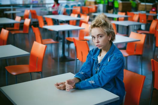 young beautiful woman in jeans clothes in business space of shopping center. portrait of a girl with freckles on her face, stylish girl in an empty cafe