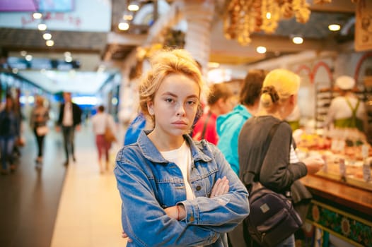 young beautiful woman in jeans clothes in business space of shopping center. portrait of a girl with freckles on her face, stylish girl standing near show-windows of fair in shopping center