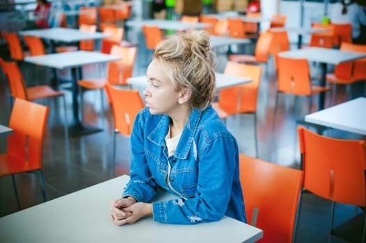 young beautiful woman in jeans clothes in business space of shopping center. portrait of a girl with freckles on her face, stylish girl in an empty cafe